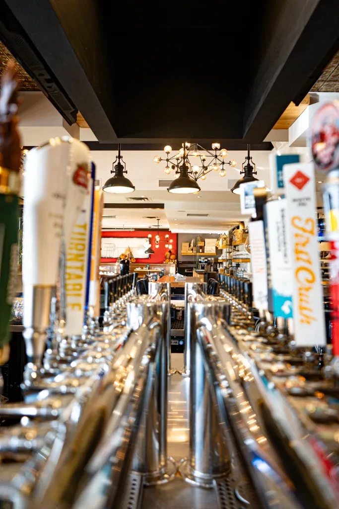 Long row of metallic beer taps in a modern bar interior.