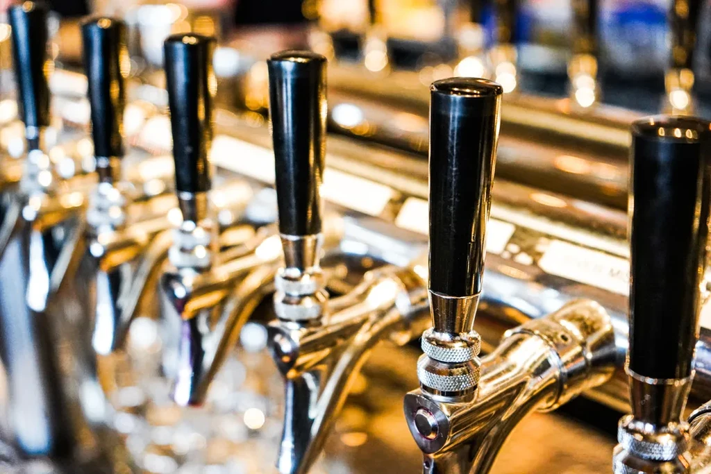 Close-up of a row of polished chrome beer taps with black handles.