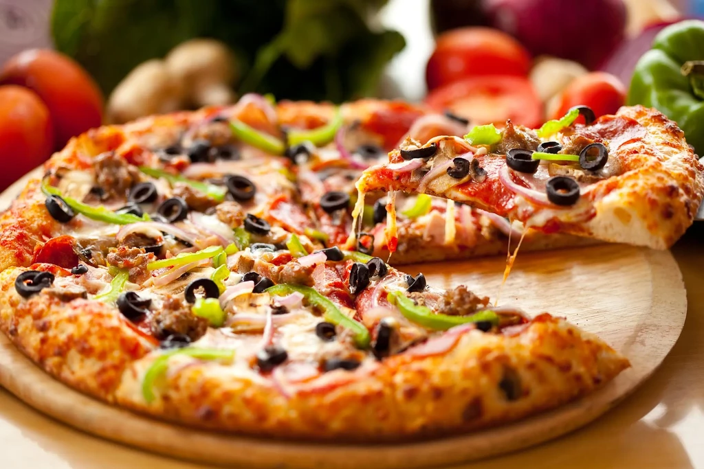 Pizza slice with stretching cheese lifted, showing olives, peppers, sausage.