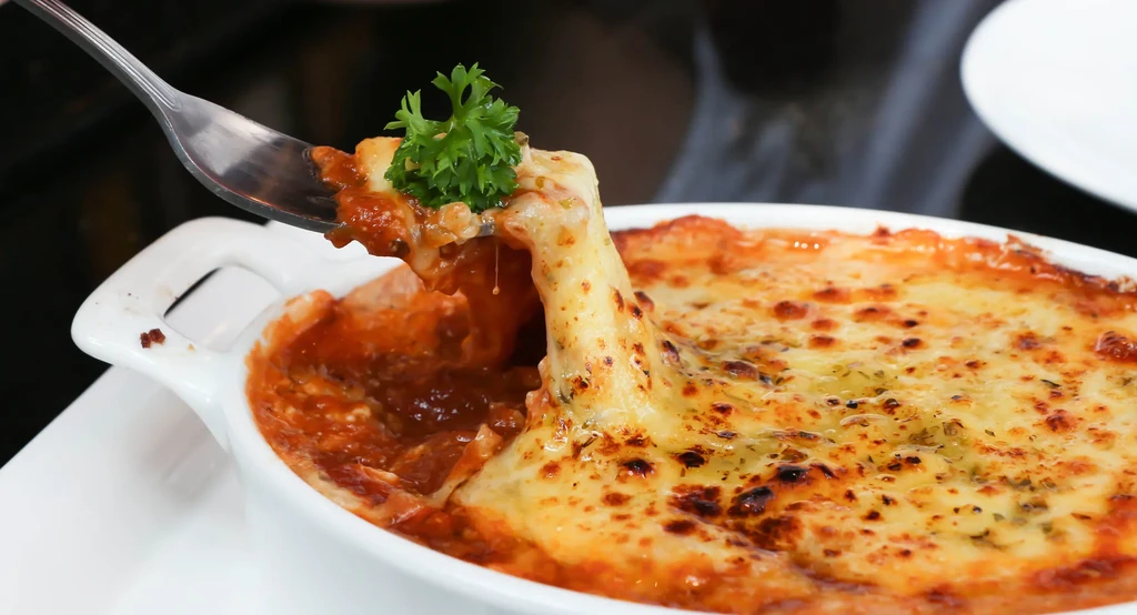 Fork lifts baked pasta, showing melted cheese stretching with herbs.