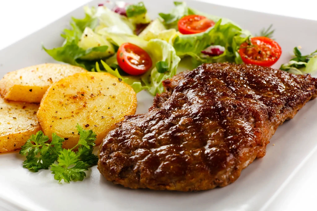 Plate of glistening steak, roasted potatoes, and fresh salad with tomatoes.