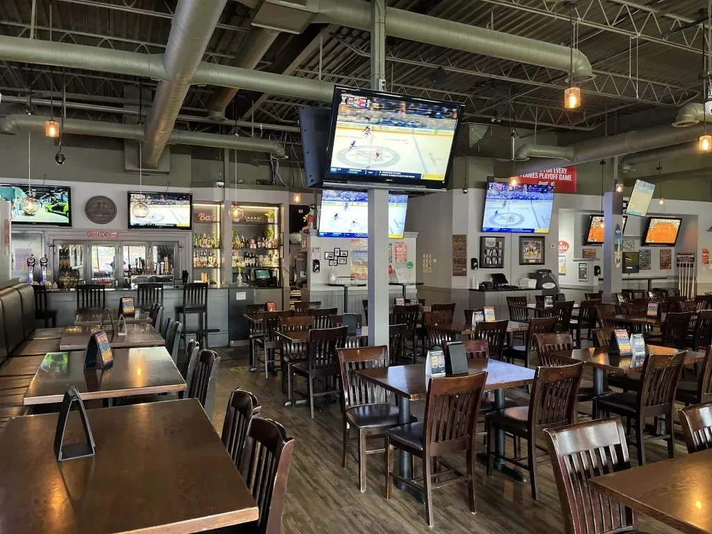 Empty sports bar with TVs showing hockey, a bar, and seating.
