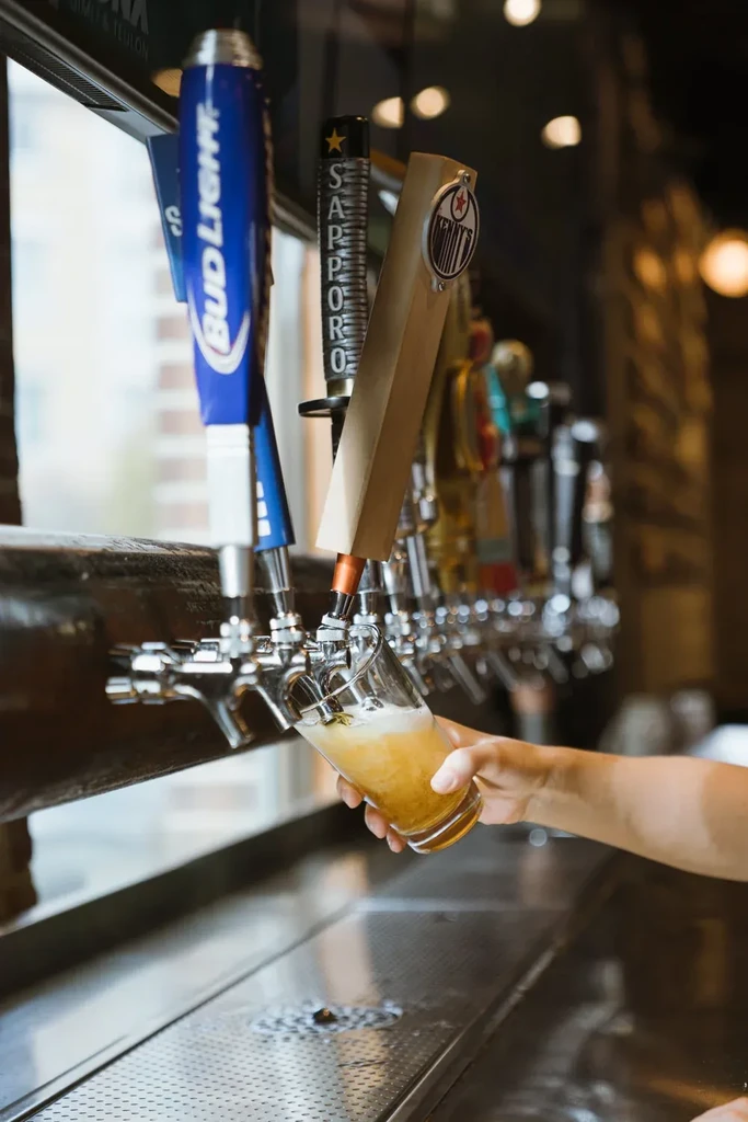 Hand pouring frothy golden beer into a glass from a bar tap.