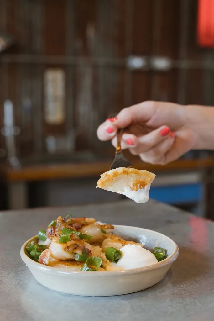 Fork lifts pierogi with sour cream and fried onions from a bowl.