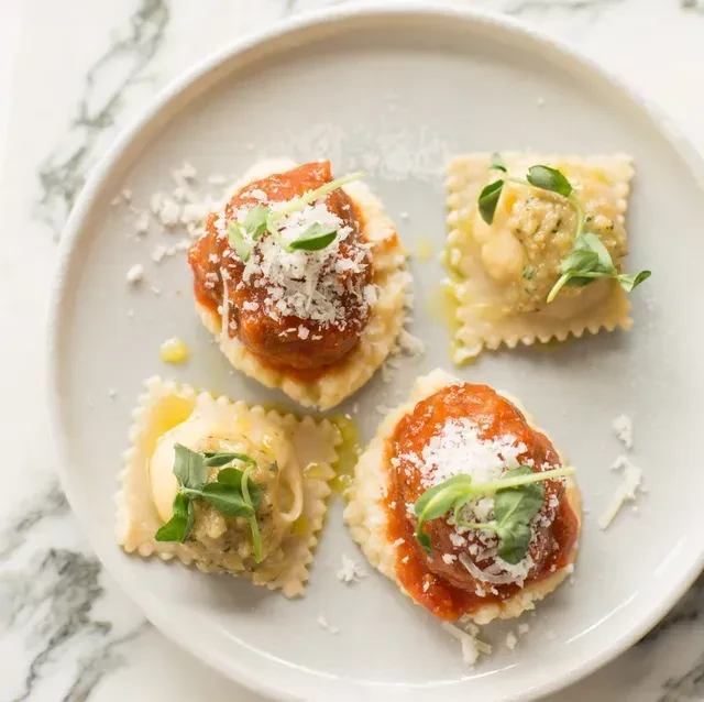 Four appetizer ravioli on a grey plate, two marinara, two creamy.