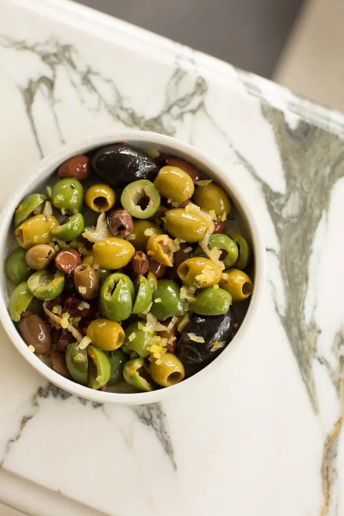 White bowl filled with colorful marinated olives on marble surface.