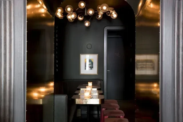 Sophisticated bar lounge, sputnik chandelier, metallic walls, and candlelit tables.