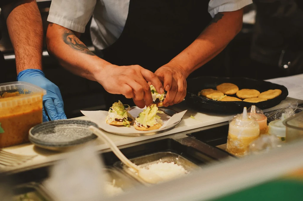 Chef's gloved and ungloved hands adding toppings to flatbreads.