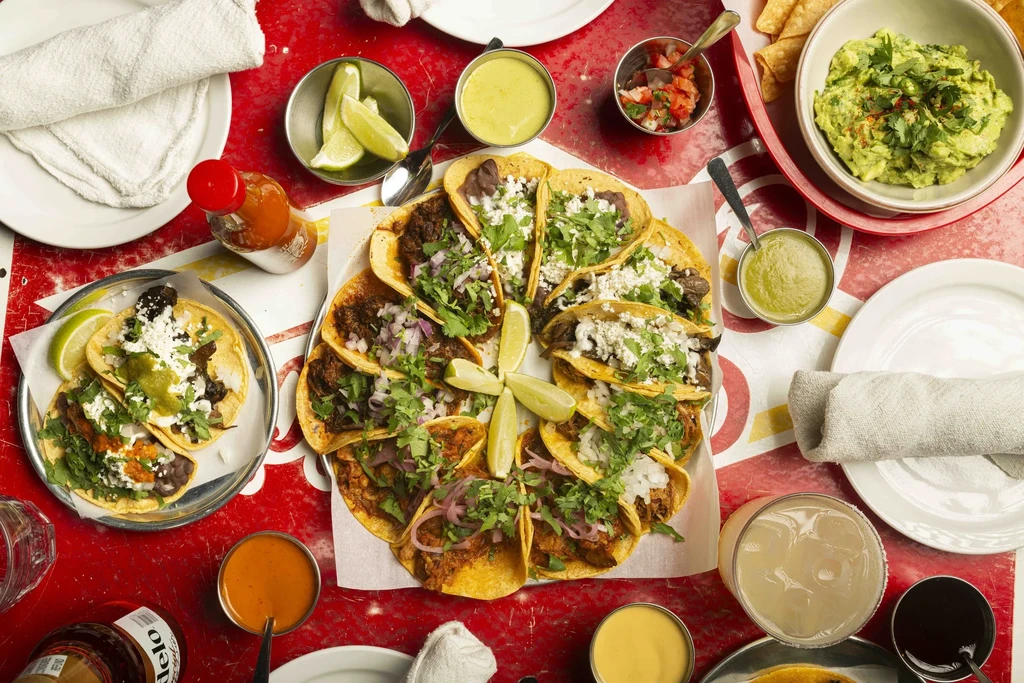 Overhead view of a red table with tacos, guacamole, and drinks.