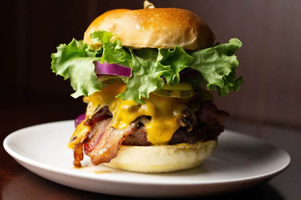 Close-up: Gourmet burger with bun, beef patty, melted cheese, bacon, lettuce, onion.