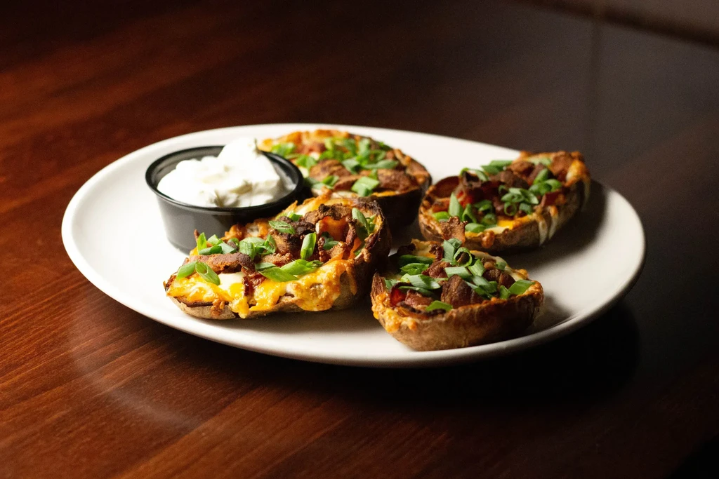 Four cheesy potato skins with bacon, green onions, and dip.