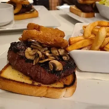 Close-up of open-faced steak sandwich, mushrooms, onion rings, and fries.