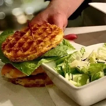 Close-up of waffle sandwich, grilled protein, lettuce, and Parmesan salad.