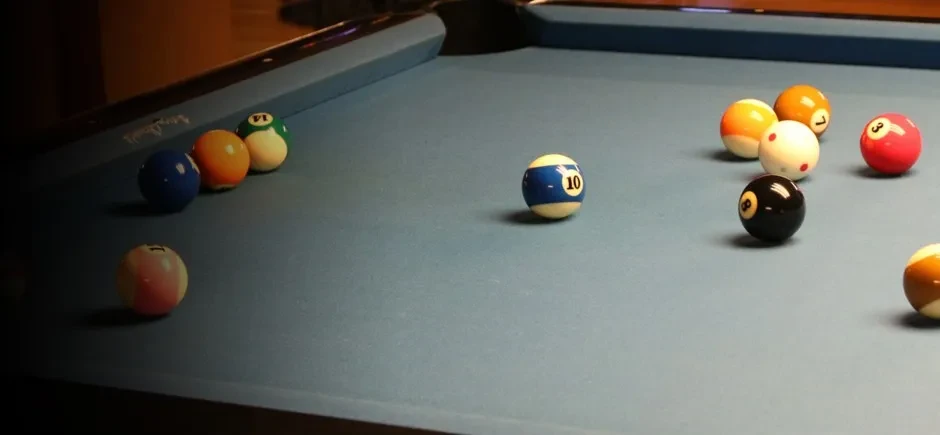 Dimly lit blue felt pool table with scattered billiard balls.