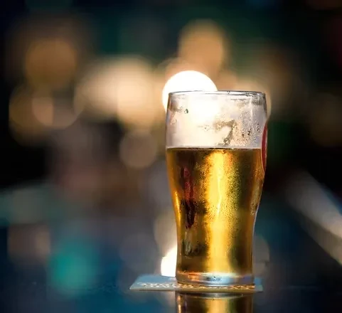 Golden beer with white foam and condensation on a bar top.