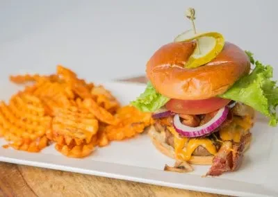 Close-up of gourmet burger with bacon, cheese, and waffle fries.