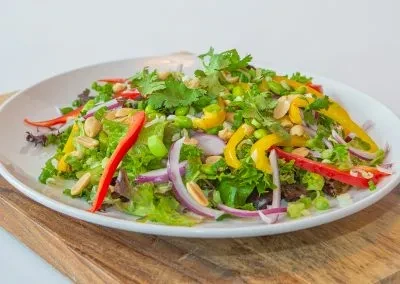 Colorful salad with greens, bell peppers, edamame, and peanuts on plate.