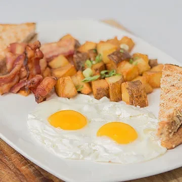 Well-plated breakfast with sunny-side-up eggs, crispy bacon, toast, and home fries.