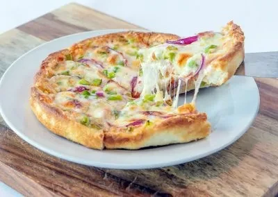 Thick-crust pizza, slice lifted with cheese pull, peppers, and onion.