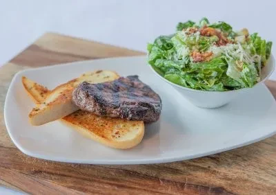 Grilled steak on toast with a side Caesar salad.
