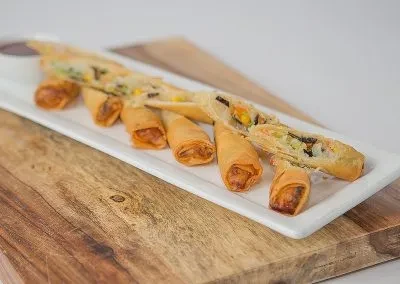 Fried golden-brown spring rolls with vegetable filling and dipping sauce.