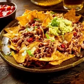 A close-up of loaded nachos with meat, cheese, and guacamole.