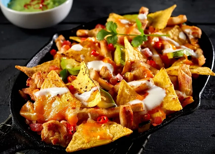 Loaded nachos in a skillet with cheese, meat, avocado, and cilantro.