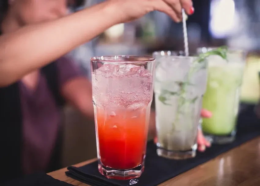 Three colorful drinks, one red-orange, being stirred at a bar.