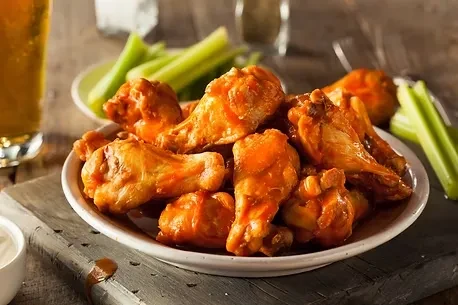 Plate of reddish-orange buffalo wings with creamy dip, celery, and beer.