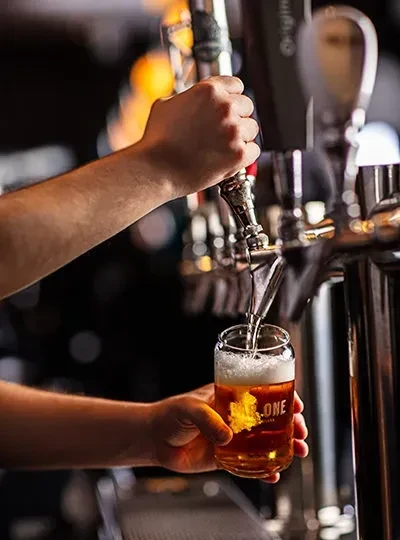 Hands pouring amber beer from a tap into a glass.