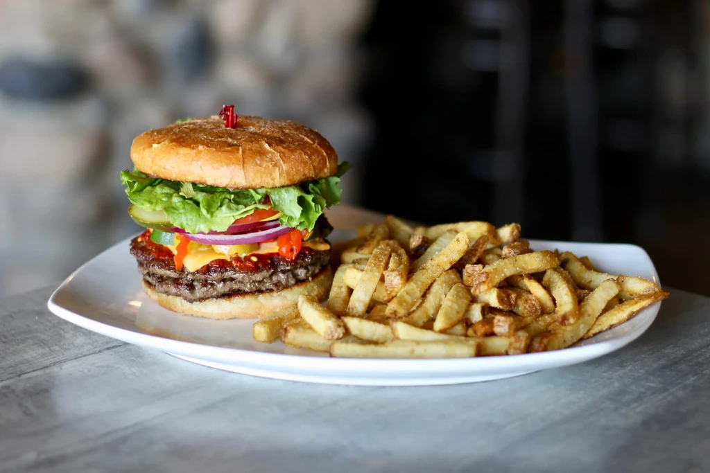 Gourmet double cheeseburger with chili relish and seasoned fries on a plate.