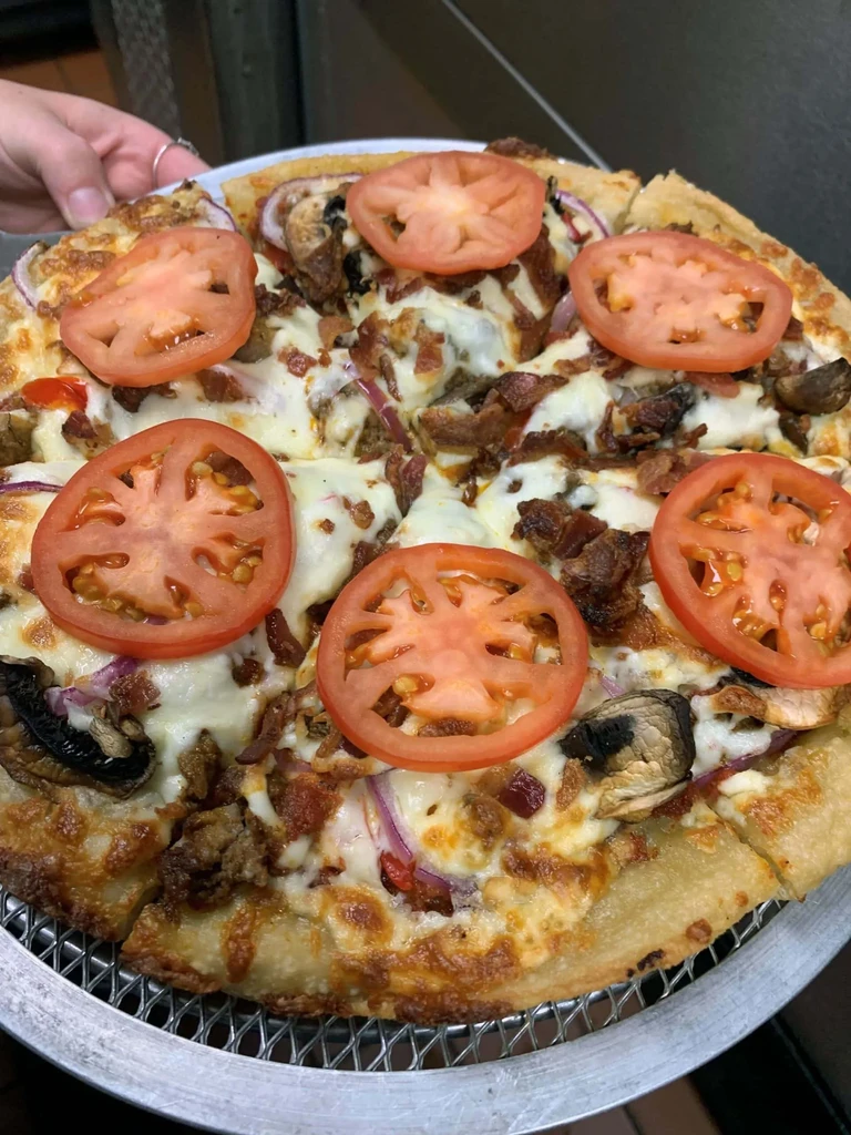 Top-down pizza: cheese, sausage, bacon, mushrooms, six bright red tomatoes.