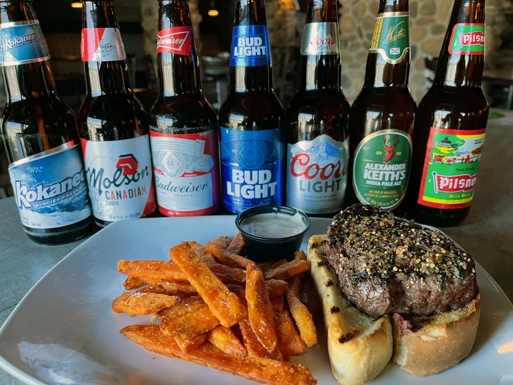 Seasoned grilled steak, sweet potato fries, creamy sauce, and various beer bottles.