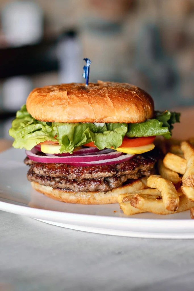 A stacked double cheeseburger and golden french fries on a white plate.