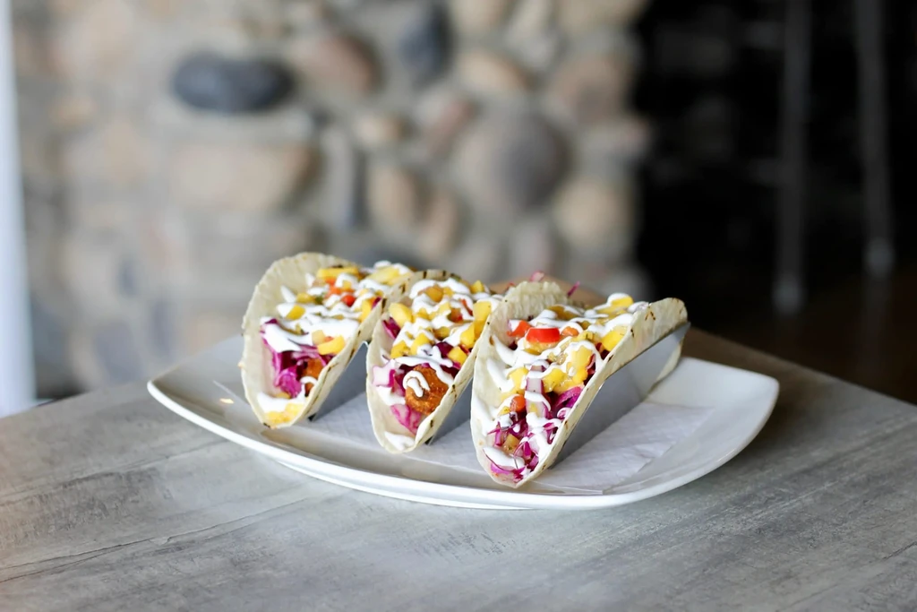 Three colorful soft tacos with purple cabbage, crispy pieces, and salsa.