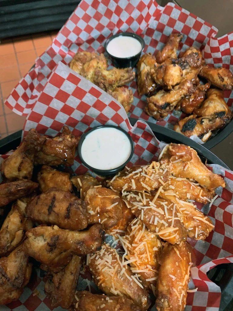 Overhead view of four types of chicken wings with dipping sauces in baskets.