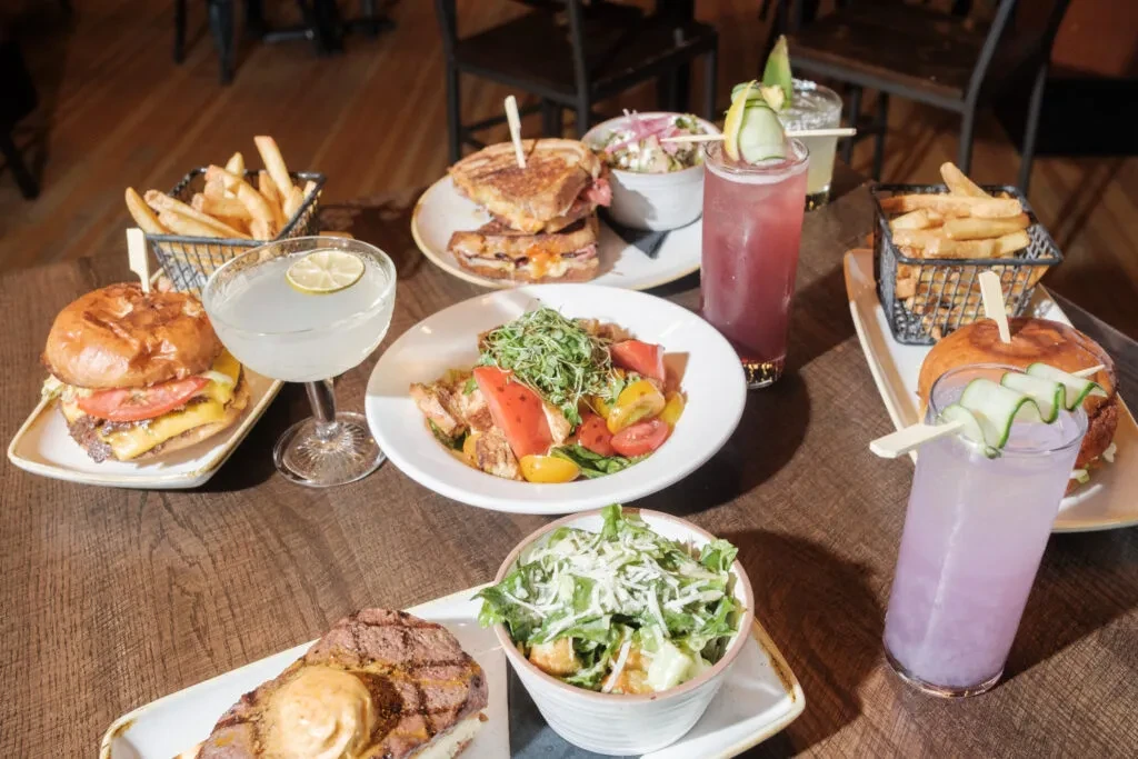 Diverse spread of burgers, fries, steak, salads, and colorful cocktails.