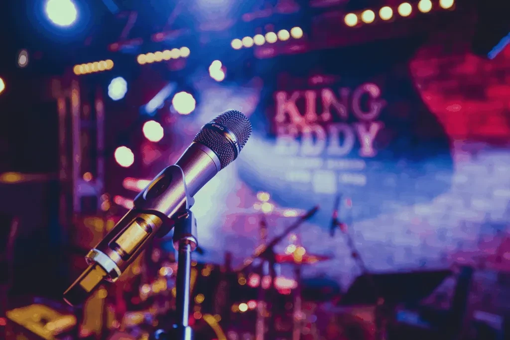 Gold microphone on stage, blurred lights, and a 'KING EDDY' sign.