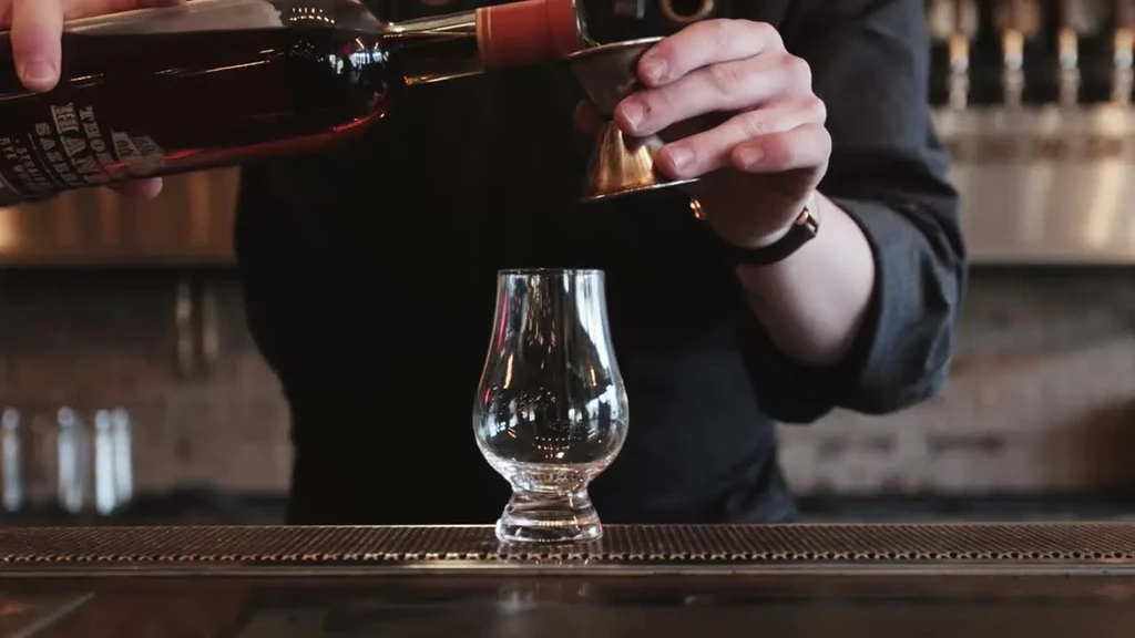 Bartender's hands pour liquid from a "THORN BARREL" bottle into a jigger.