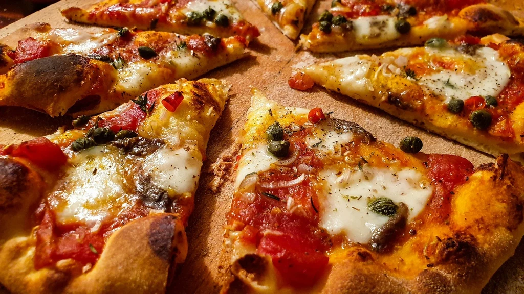 Close-up of pizza slices with melted cheese, capers, peppers, and herbs.