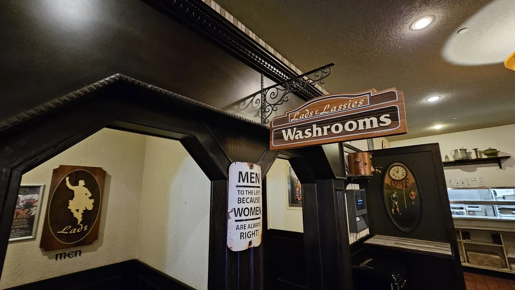 Dark wood washroom archway with "Lads & Lassies" and humorous signs.