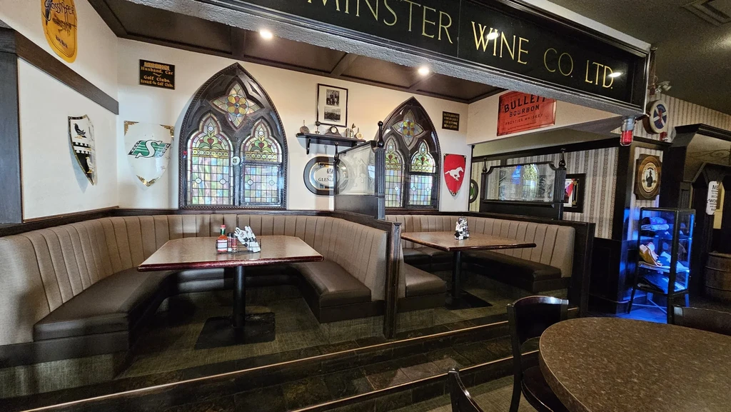 Empty traditional pub interior with booths, dark wood, and stained-glass windows.