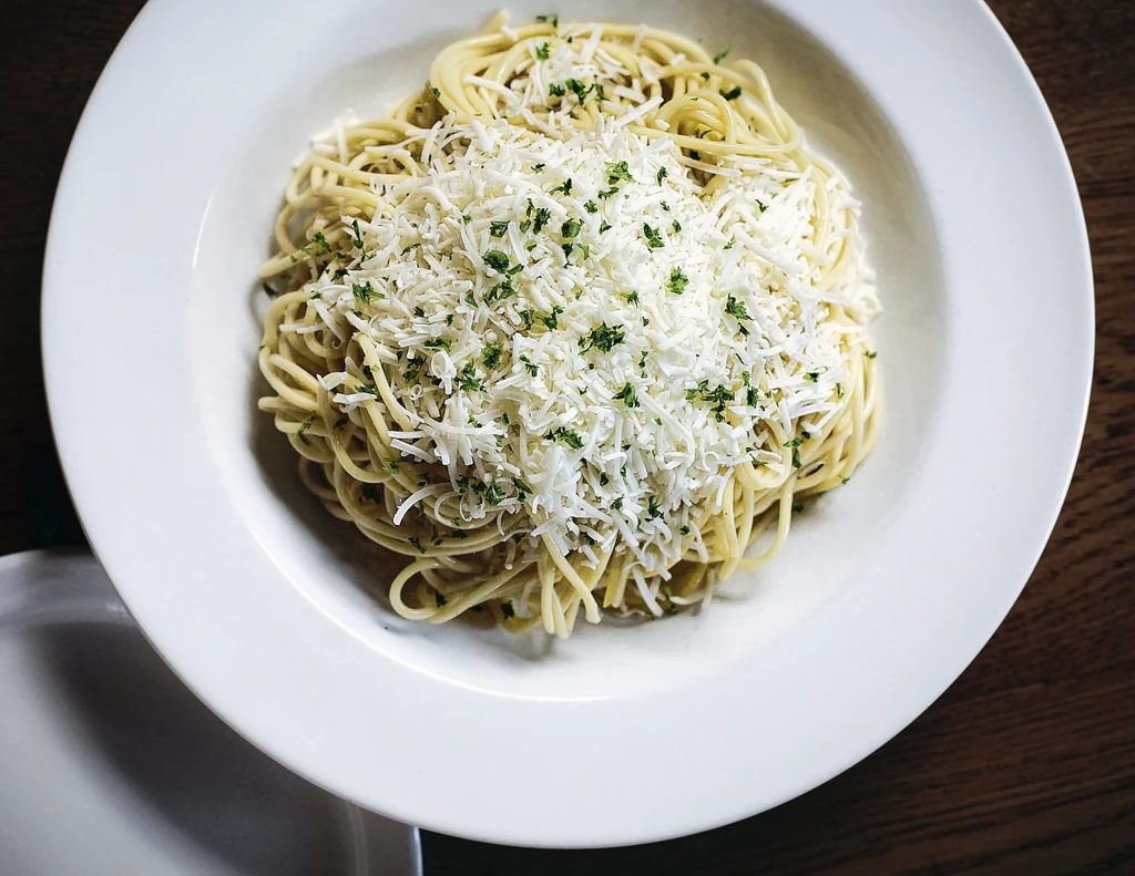 Spaghetti topped with grated cheese and green herbs in a white bowl.