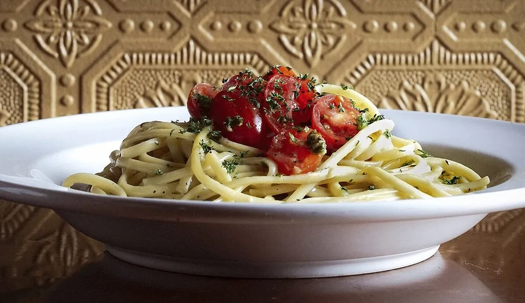 Pasta dish with halved red tomatoes and green herbs in a bowl.