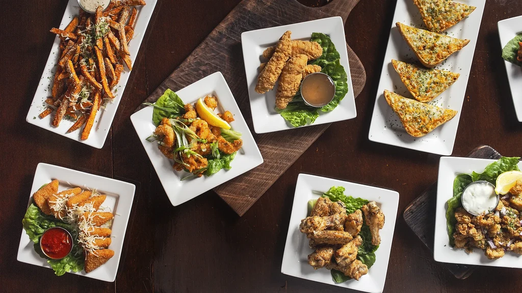 Seven different appetizers including fries, wings, and fried seafood, overhead.