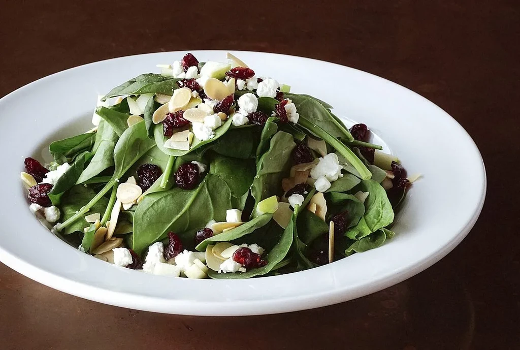 Fresh spinach salad with cranberries, cheese, almonds, and apple.