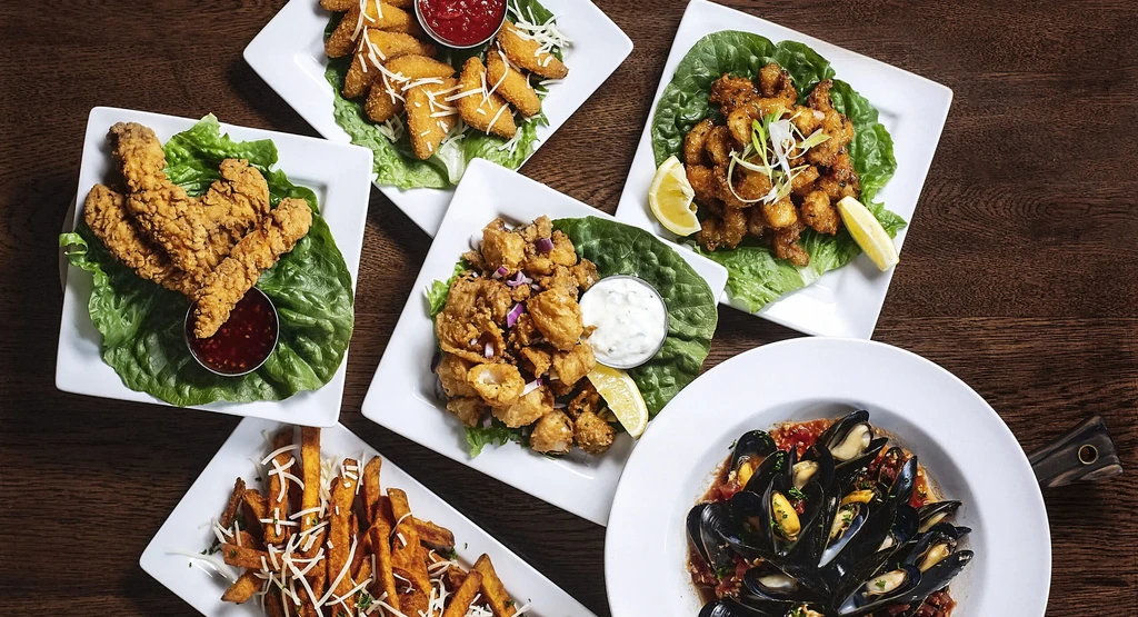 Overhead shot of six diverse appetizer and main dishes on a table.