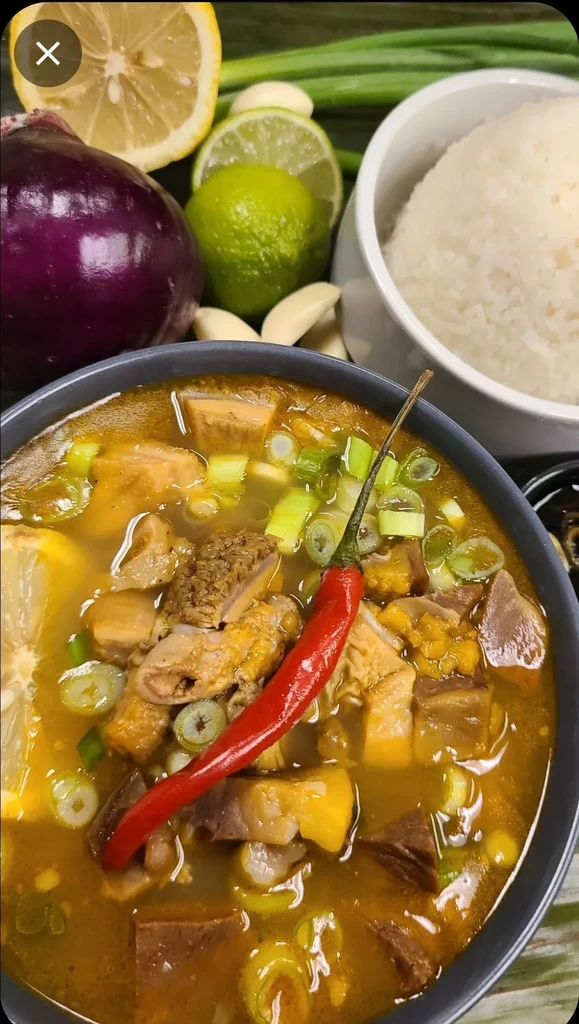 Vibrant bowl of meat and tripe soup with chili, lemon, rice, garnishes.