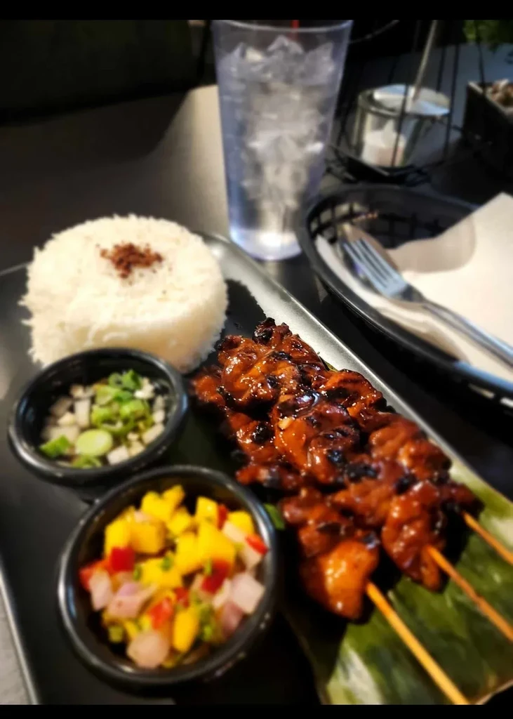 Grilled meat skewers on banana leaf with rice and colorful salsa.