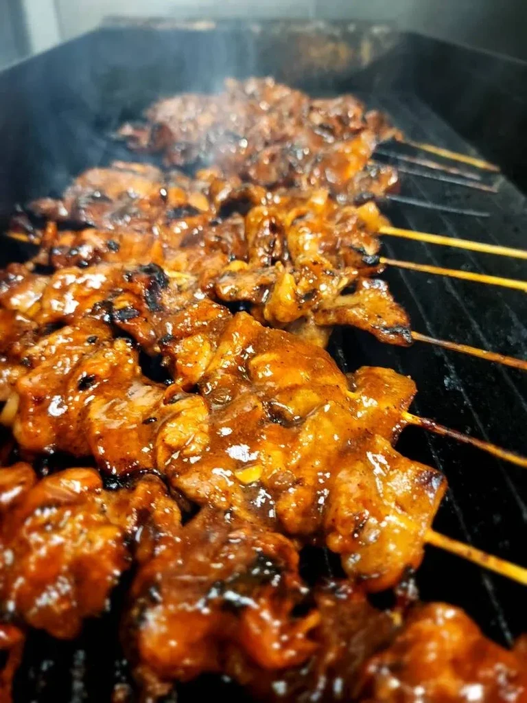 Reddish-brown marinated meat skewers grilling on a dark grate.